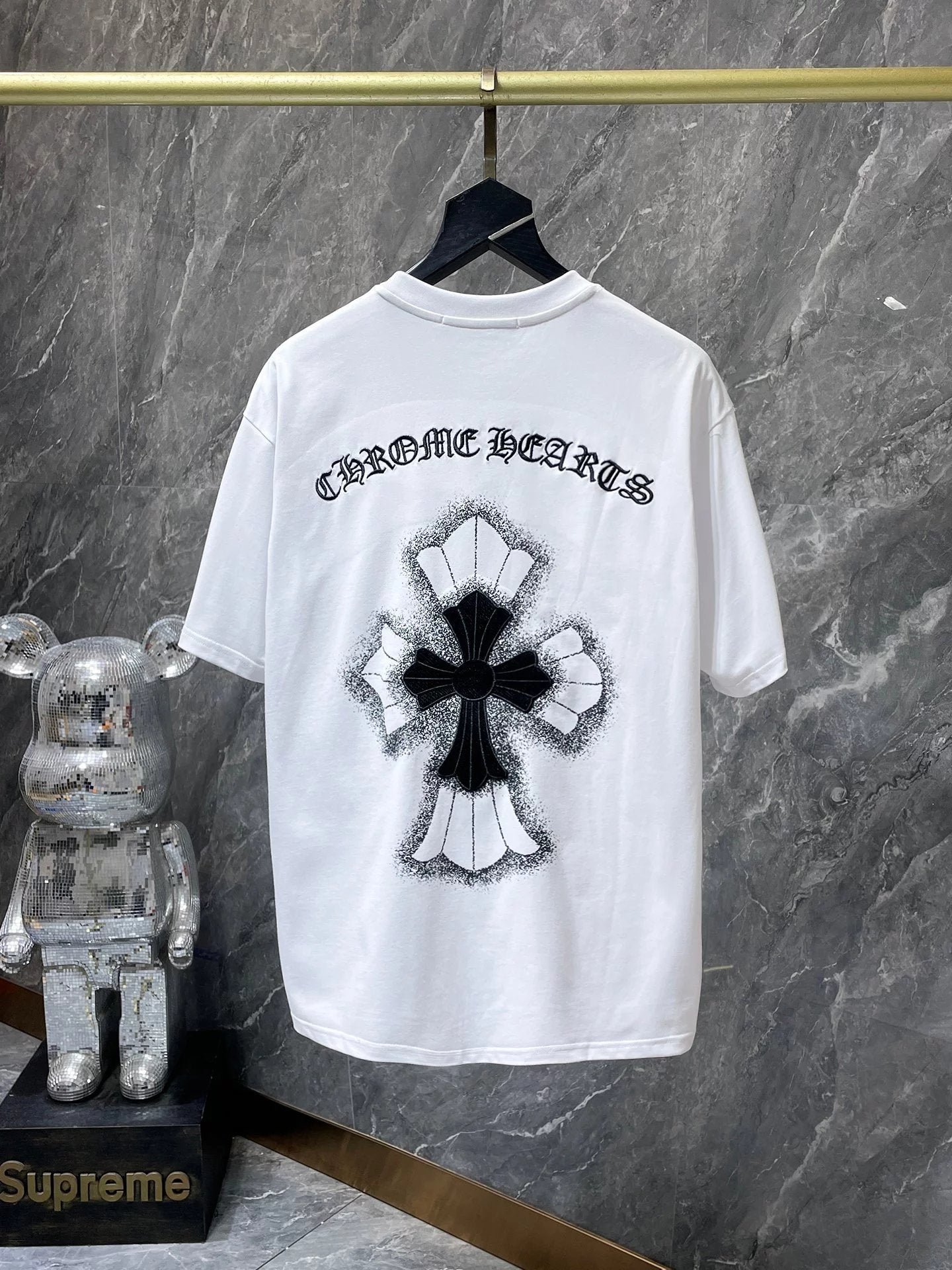 White t-shirt with black graphic design and text on a hanger against a gray marble wall.