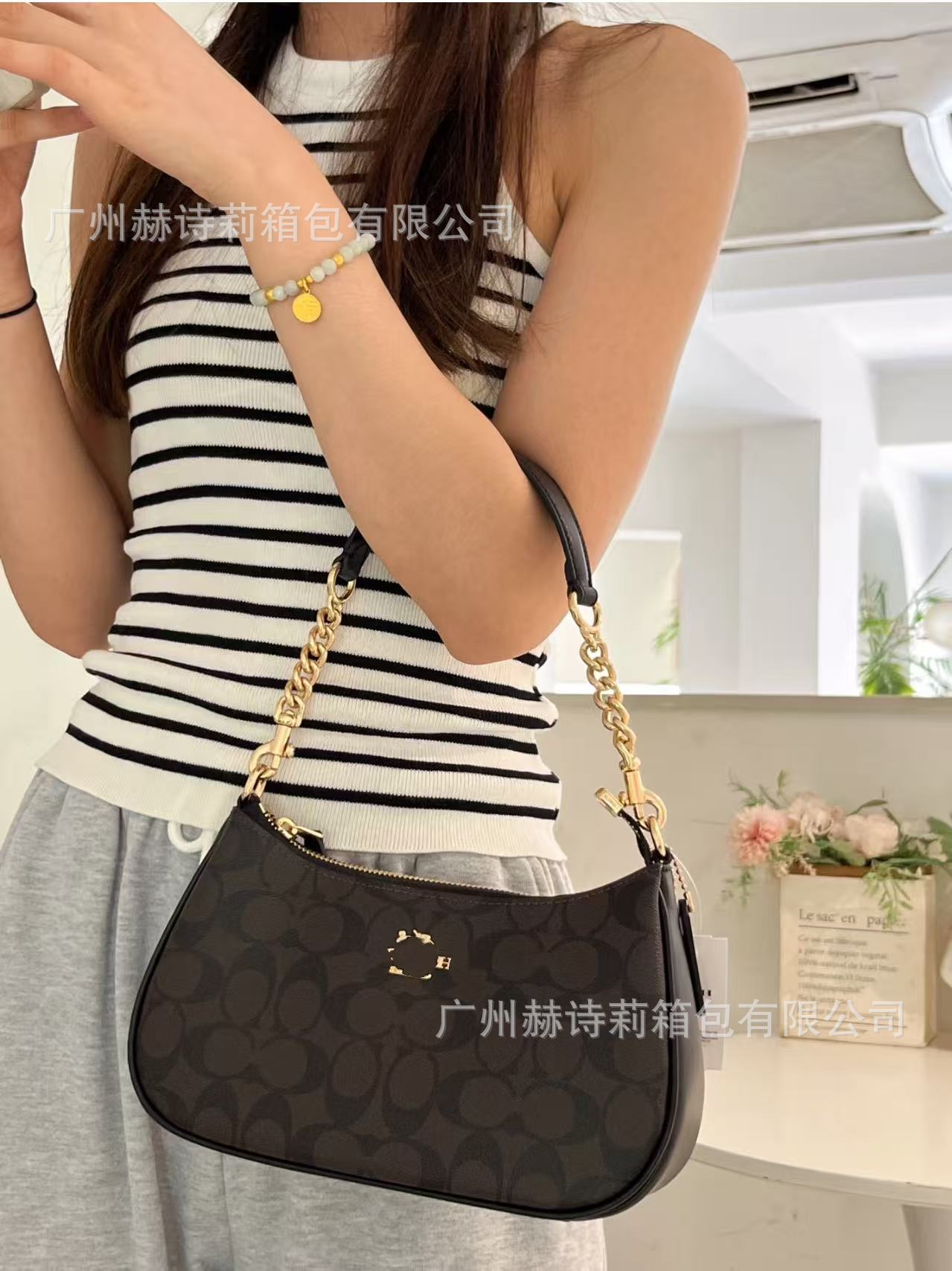 Person holding a black handbag with a gold chain strap indoors.