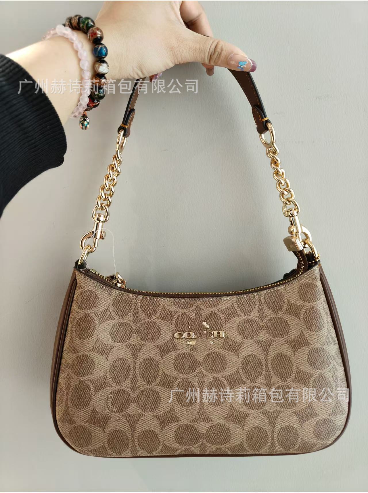 Brown handbag with gold chain handle held by a person against a gray background
