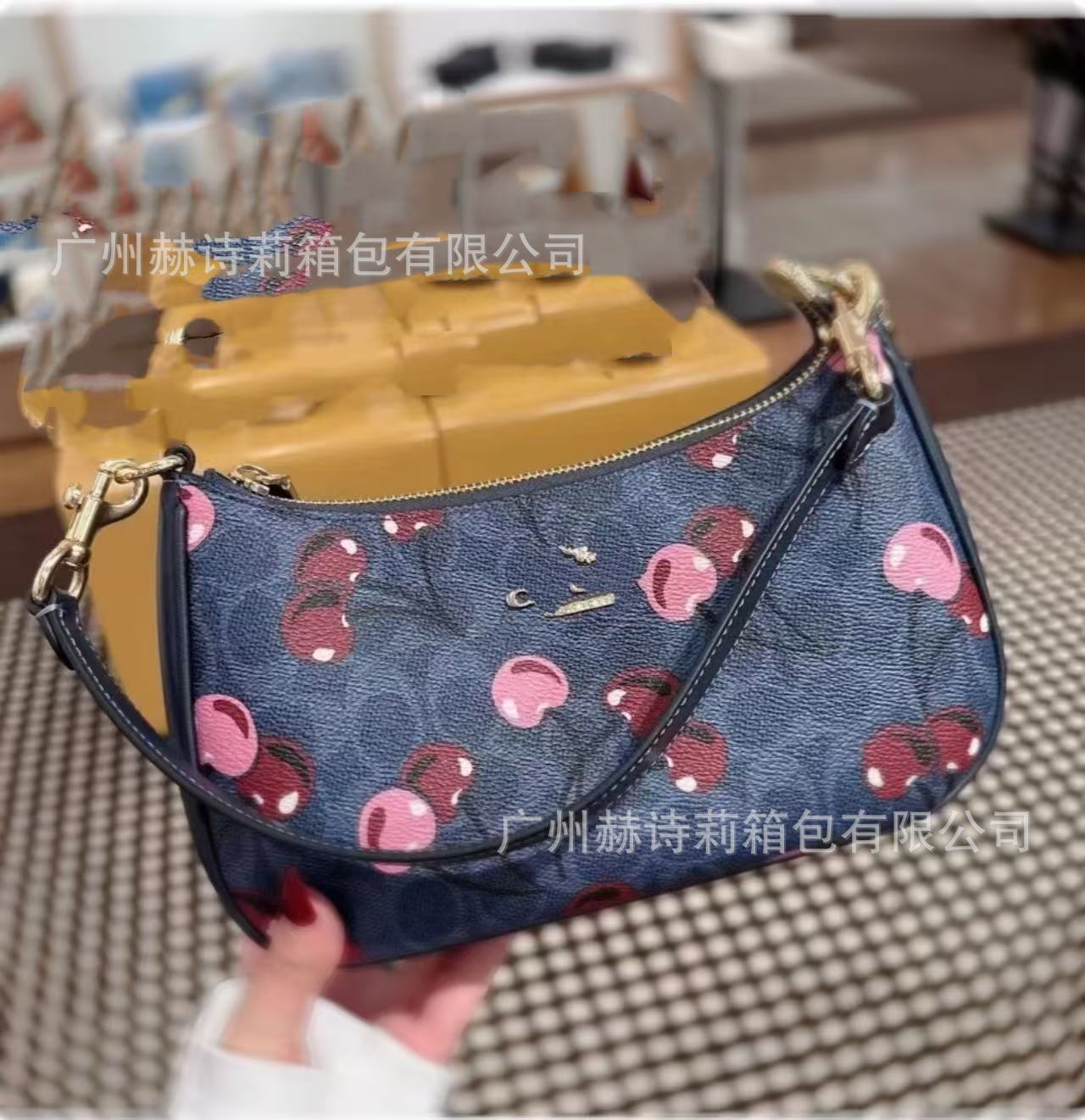 Blue handbag with pink cherry pattern held by a person, blurred background