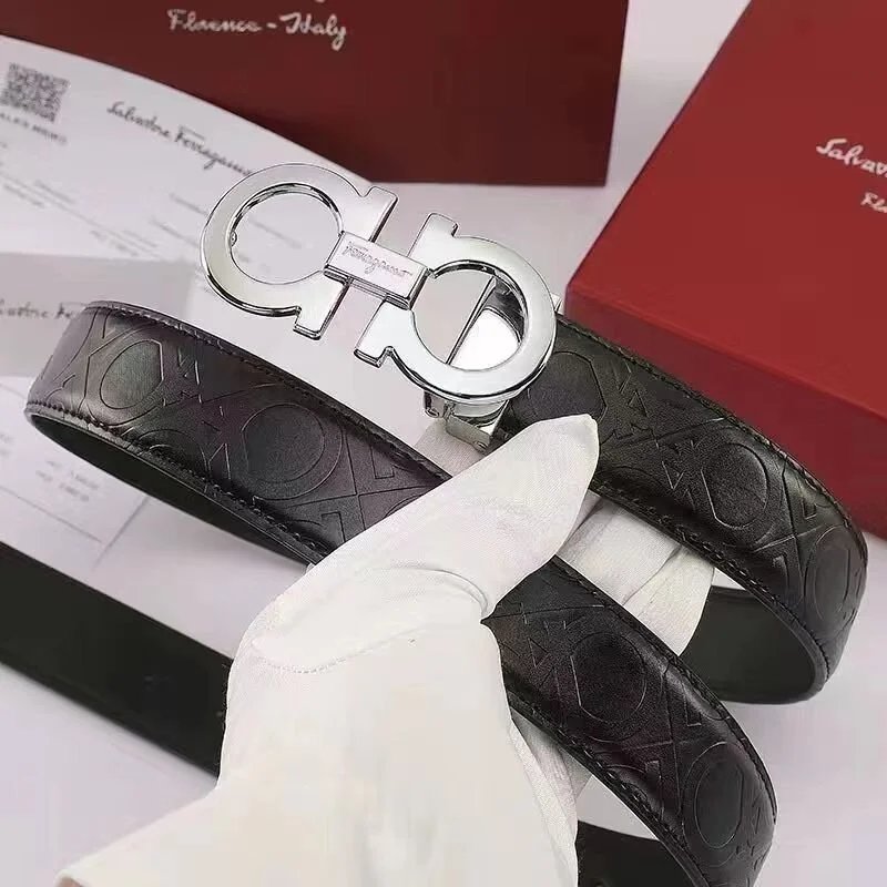 Black leather belt with silver Ferragamo buckle held by a gloved hand, with brand packaging in the background.