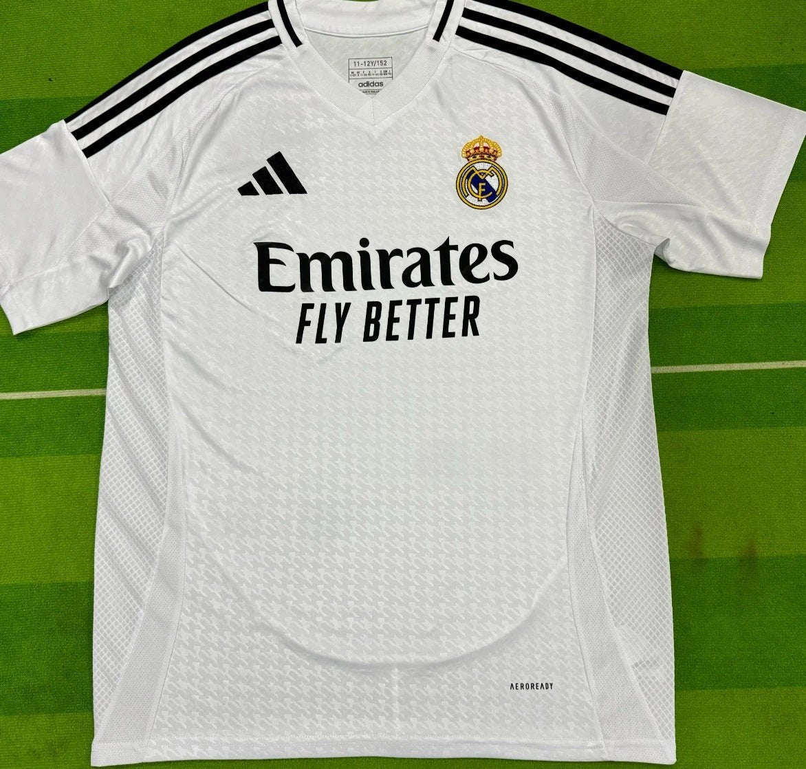 White sports jersey with Adidas and Real Madrid logos on a green background