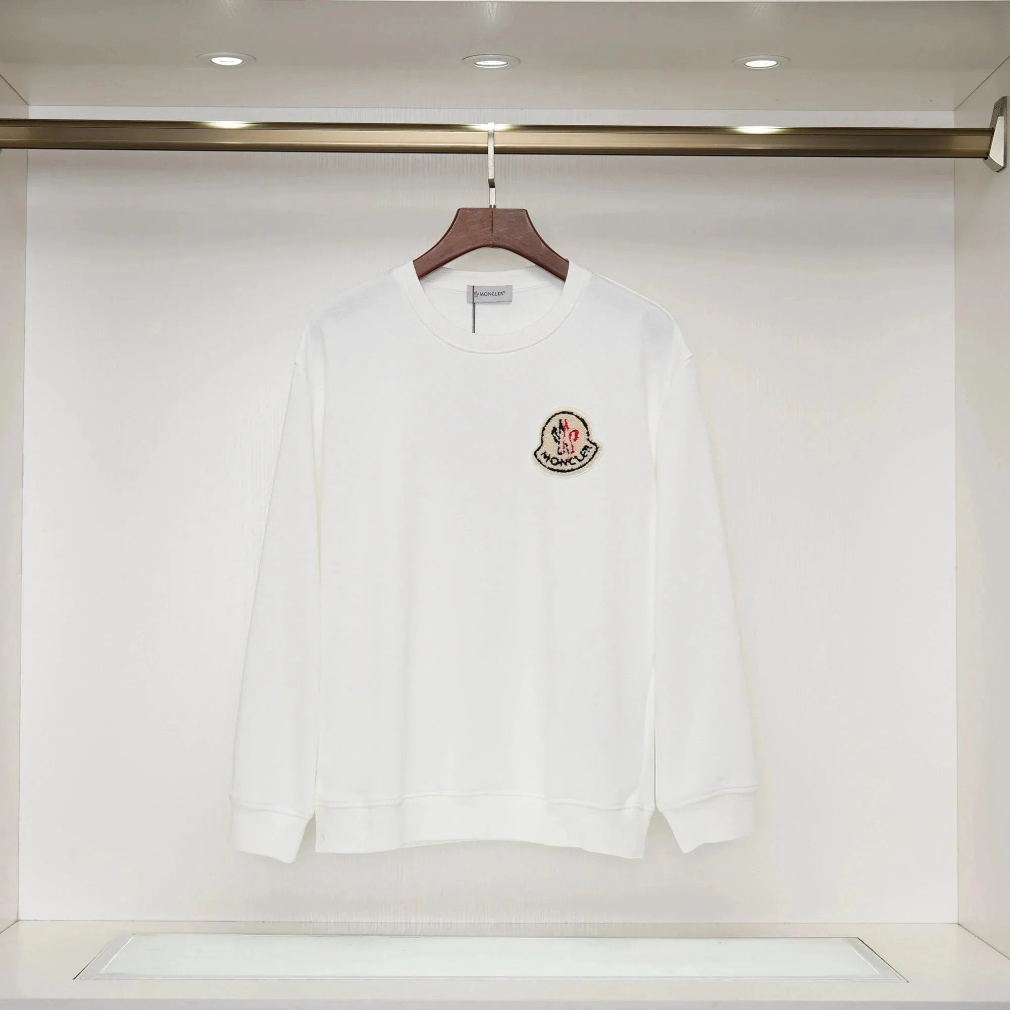 White long-sleeve shirt with a logo on a hanger against a white background