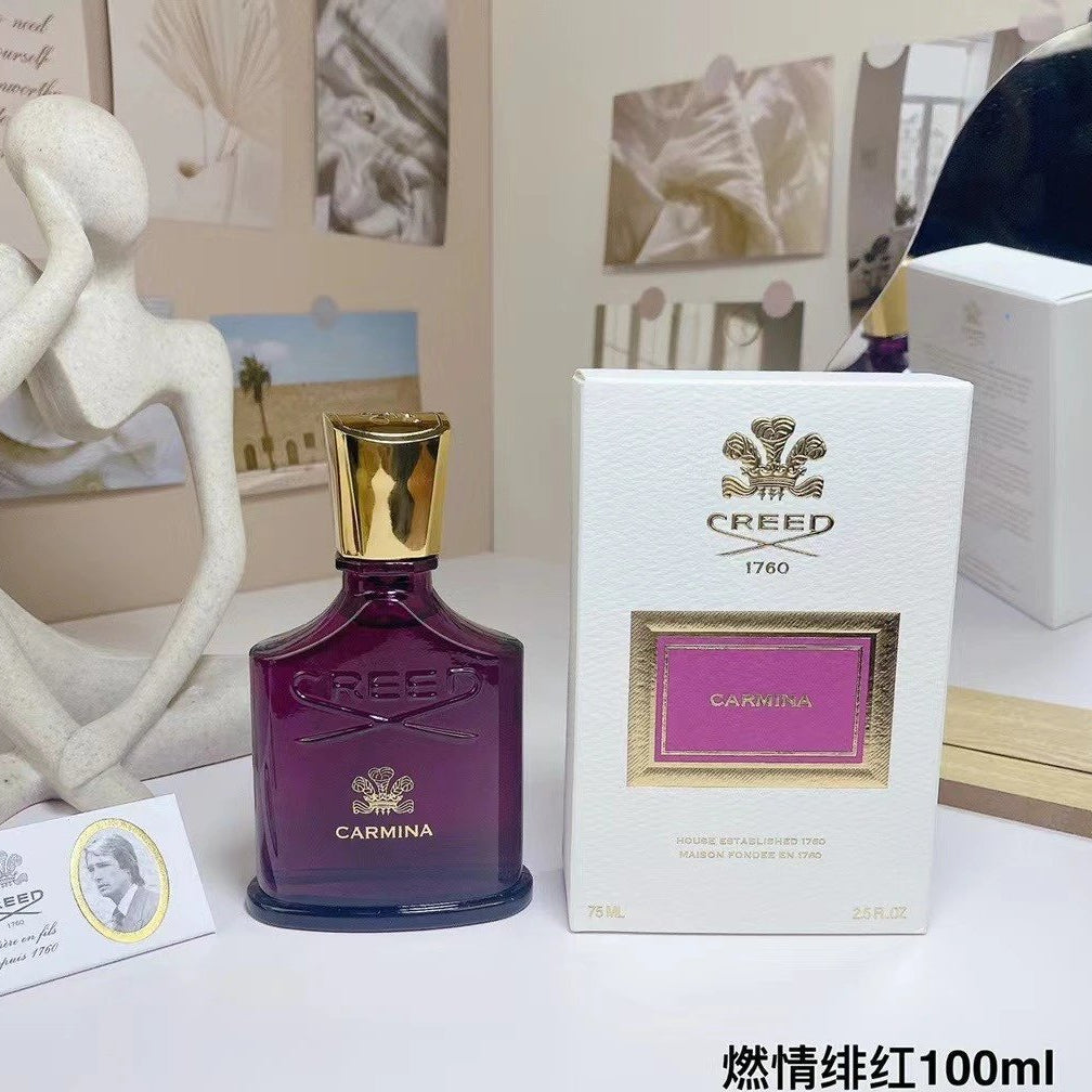 Creed Carmina perfume bottle and packaging on a table with decorative items.