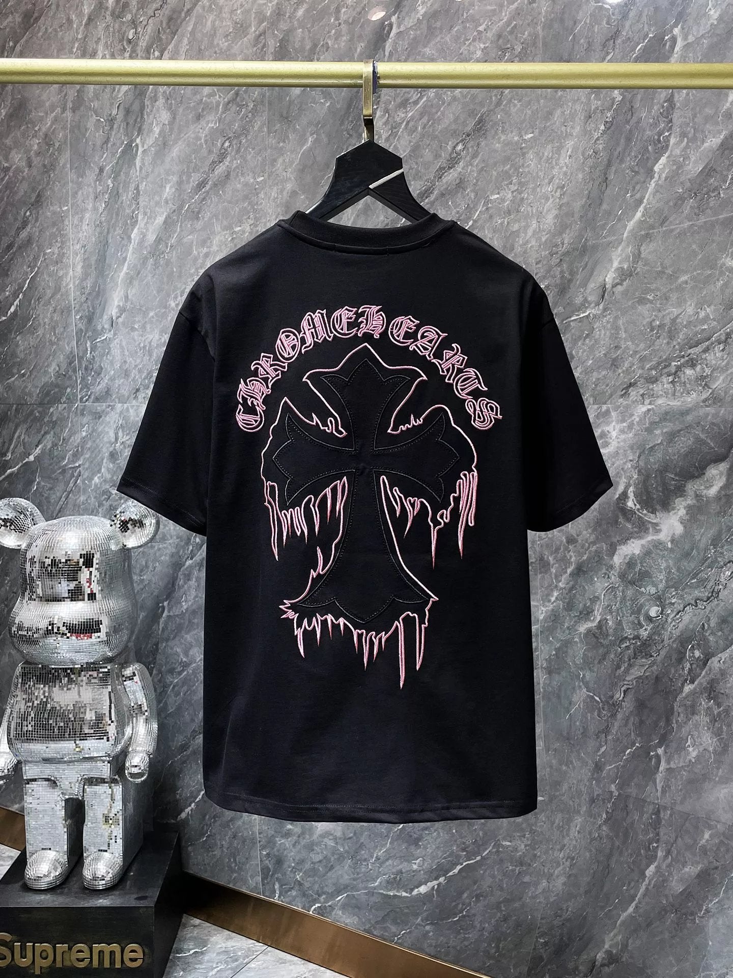 Black t-shirt with graphic design and text on a hanger against a gray marble wall.