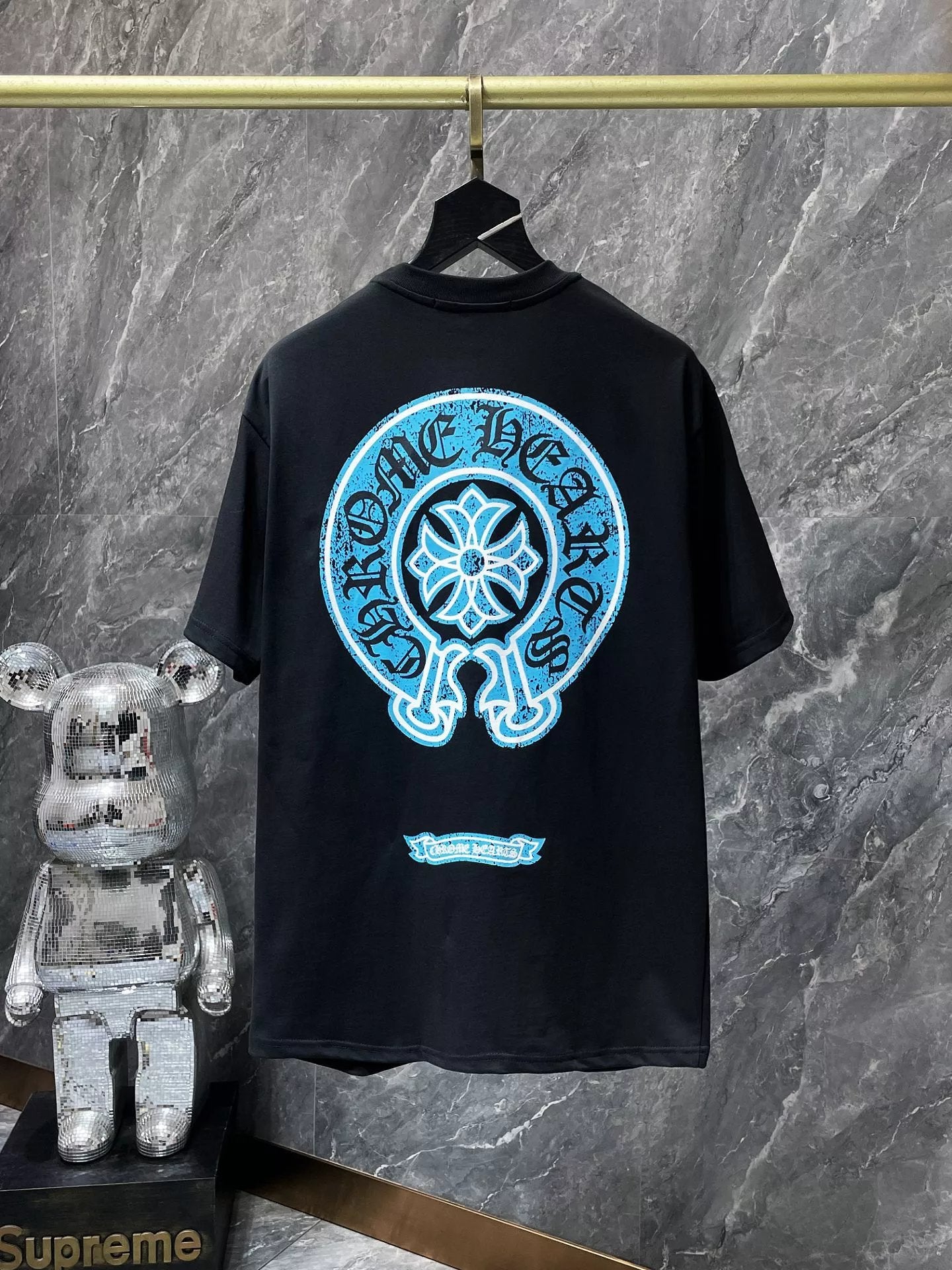Black t-shirt with blue graphic design on a hanger against a gray marble wall.