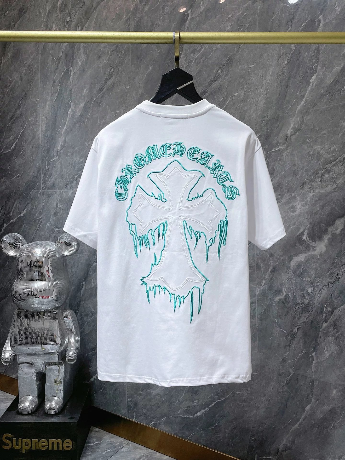 White t-shirt with green graphic design on a hanger against a marble wall.