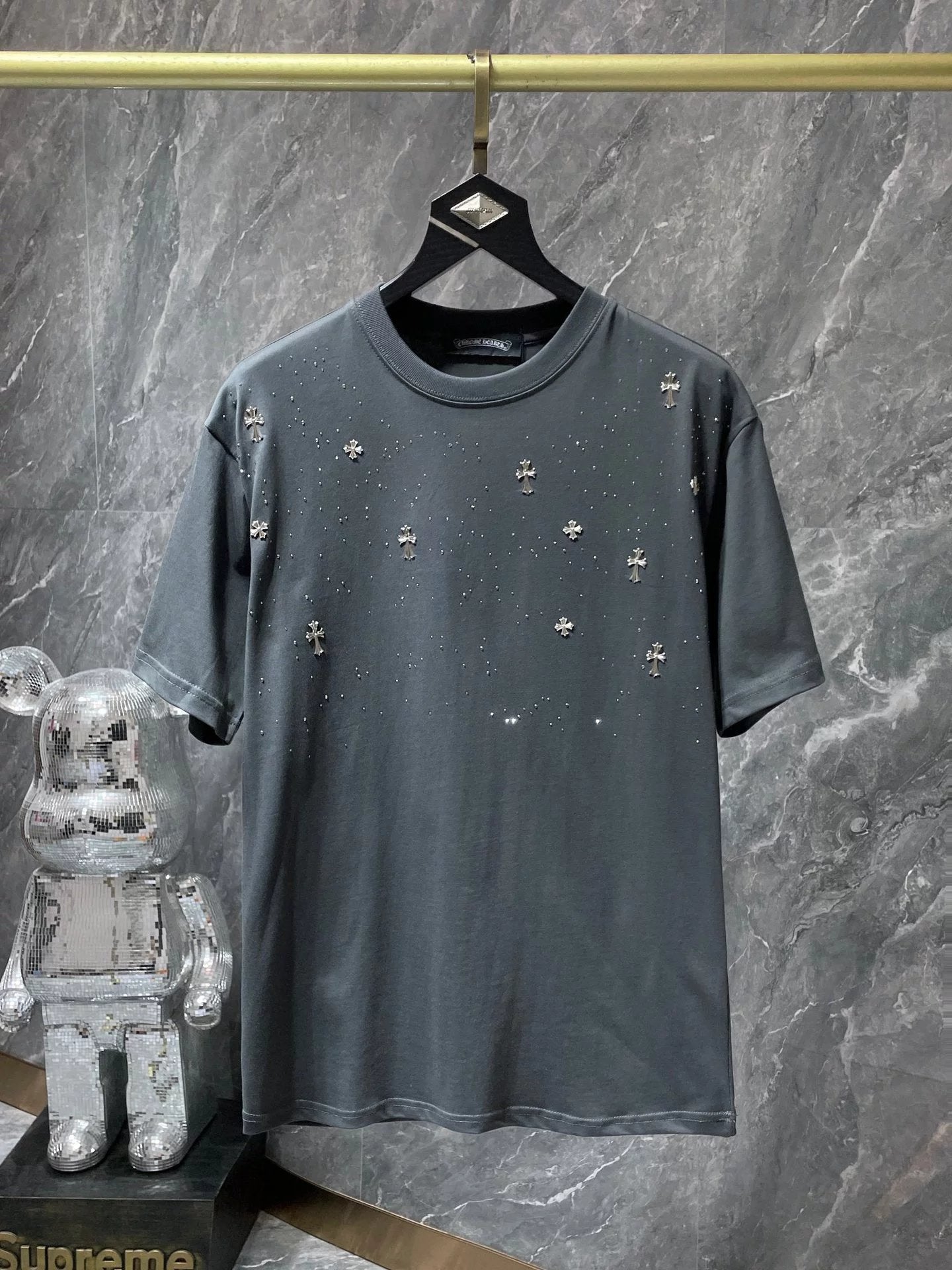 Gray t-shirt with small crosses on a hanger against a gray marble wall.