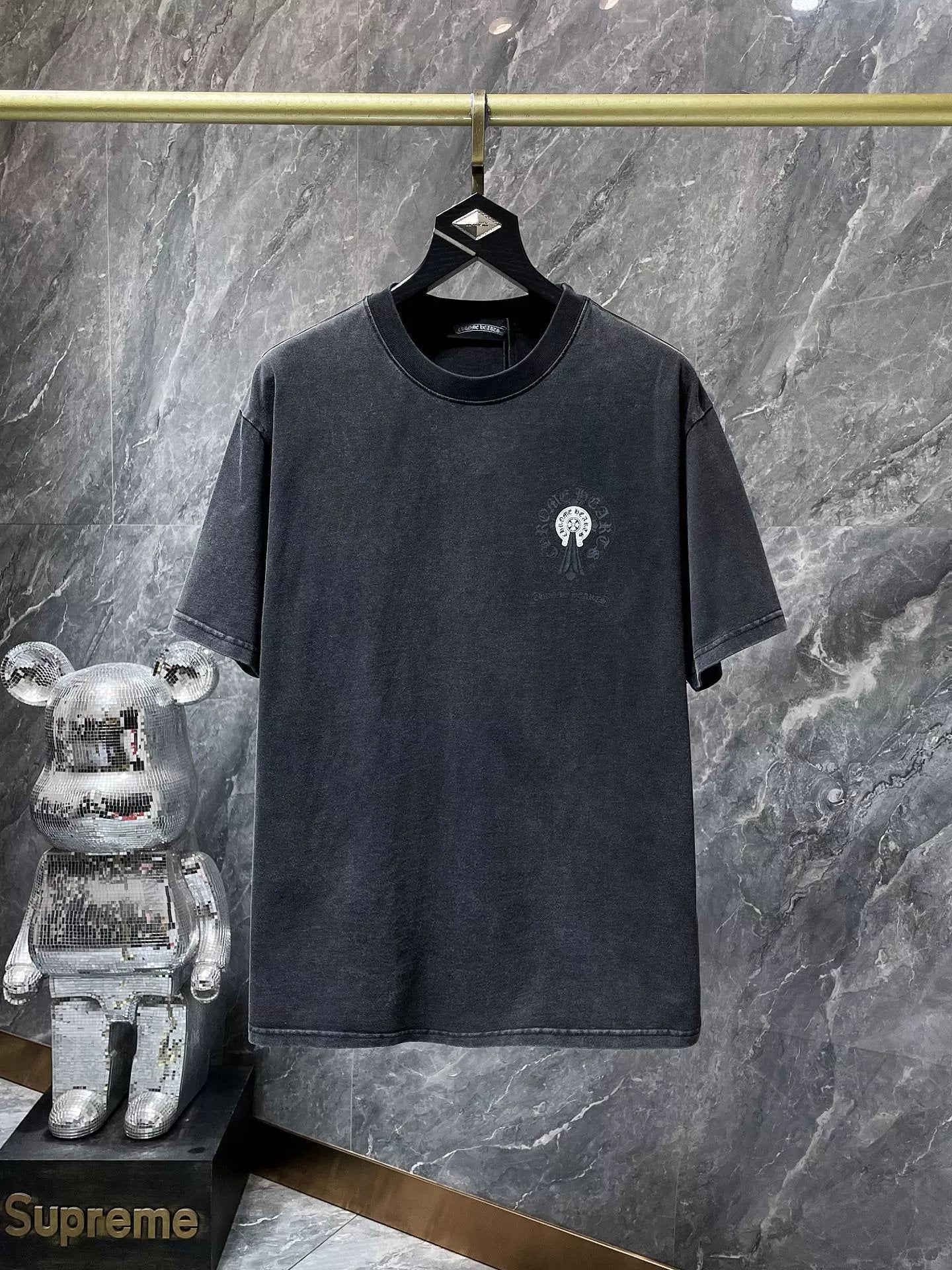 Black t-shirt with a logo on a hanger against a marble wall, with 'Supreme' branding visible.