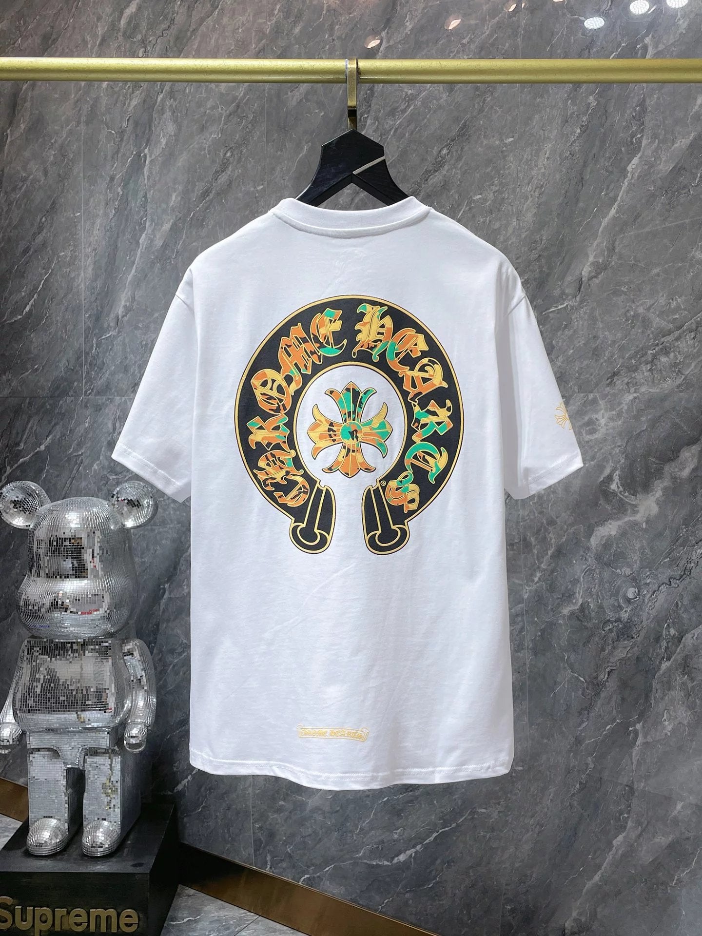 White t-shirt with a colorful graphic design on a hanger against a marble wall.