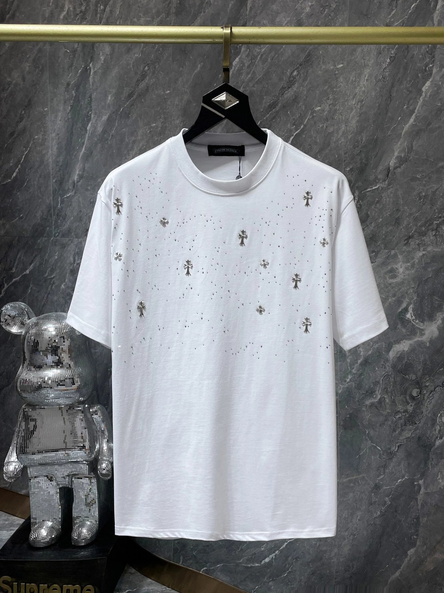 White t-shirt with small decorative patterns on a hanger against a gray marble background.