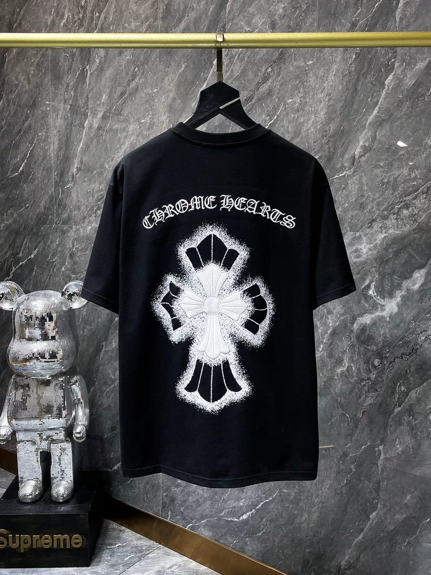 Black t-shirt with white graphic design on a hanger against a gray marble wall.