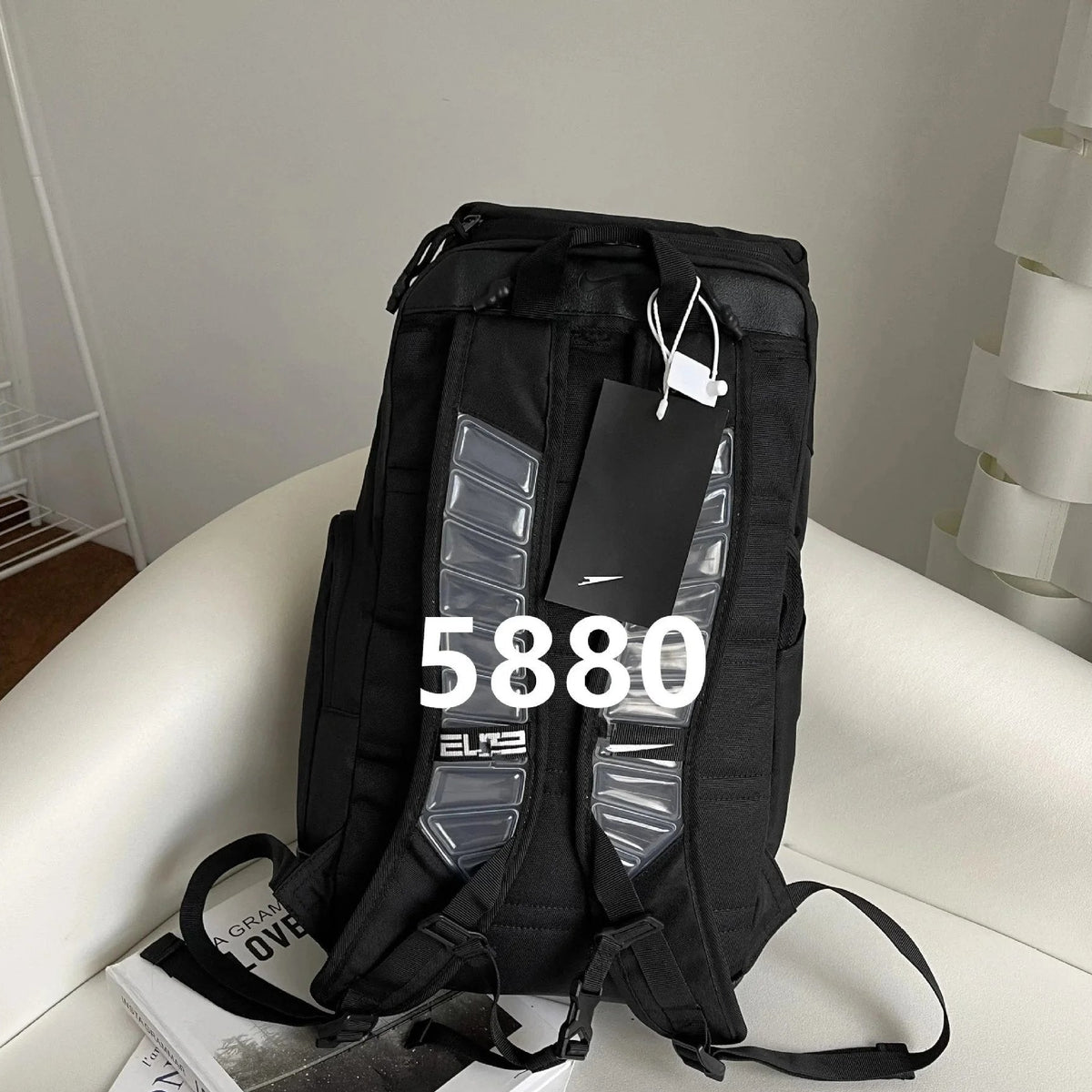A black Nike backpack with gray textured side panels, resting on a white leather sofa with a price overlay of 5880.