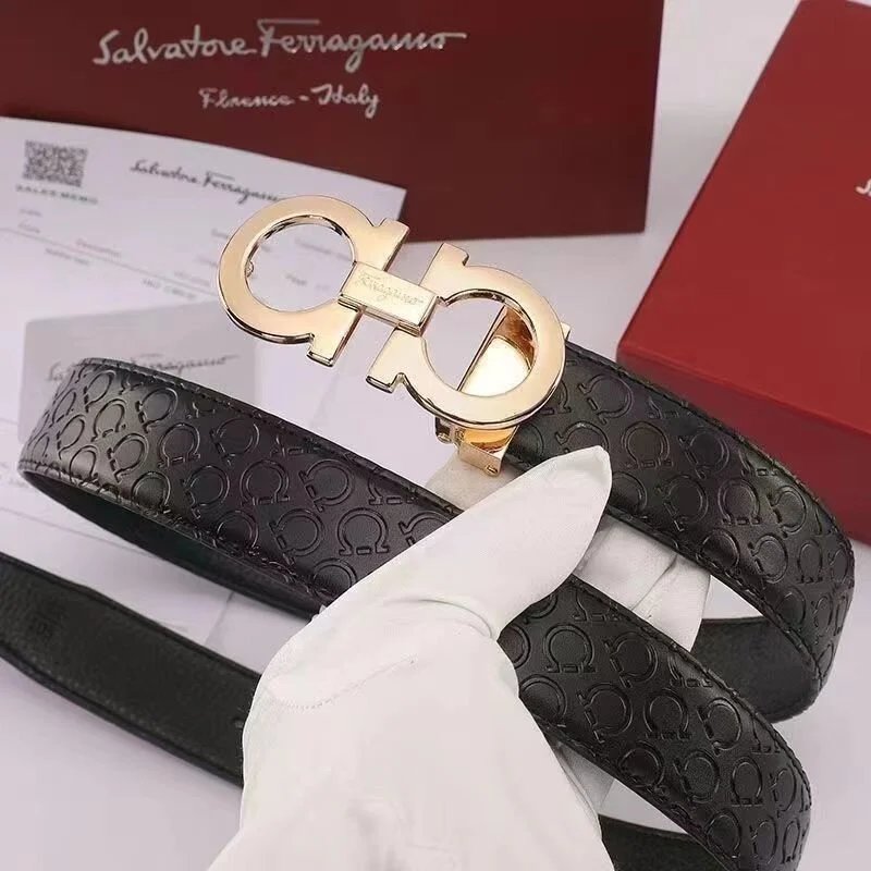 Black leather belt with gold Ferragamo Gancini buckle held by a gloved hand on a white background.