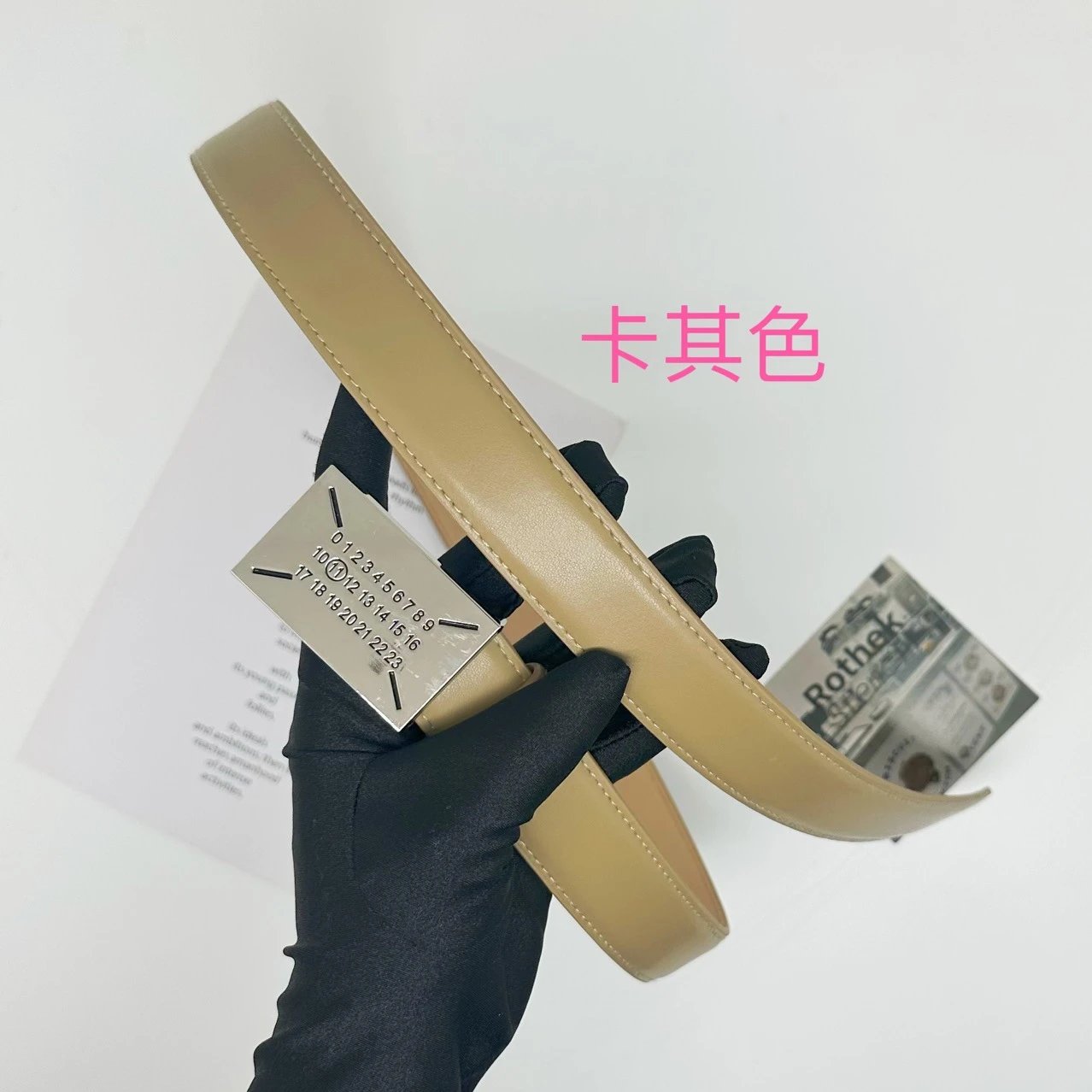 Beige belt with a brand tag held by a gloved hand on a white background