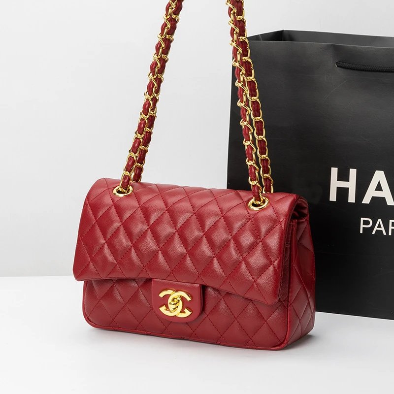 Red quilted handbag with gold chain strap and clasp, placed against a black Harrods bag.