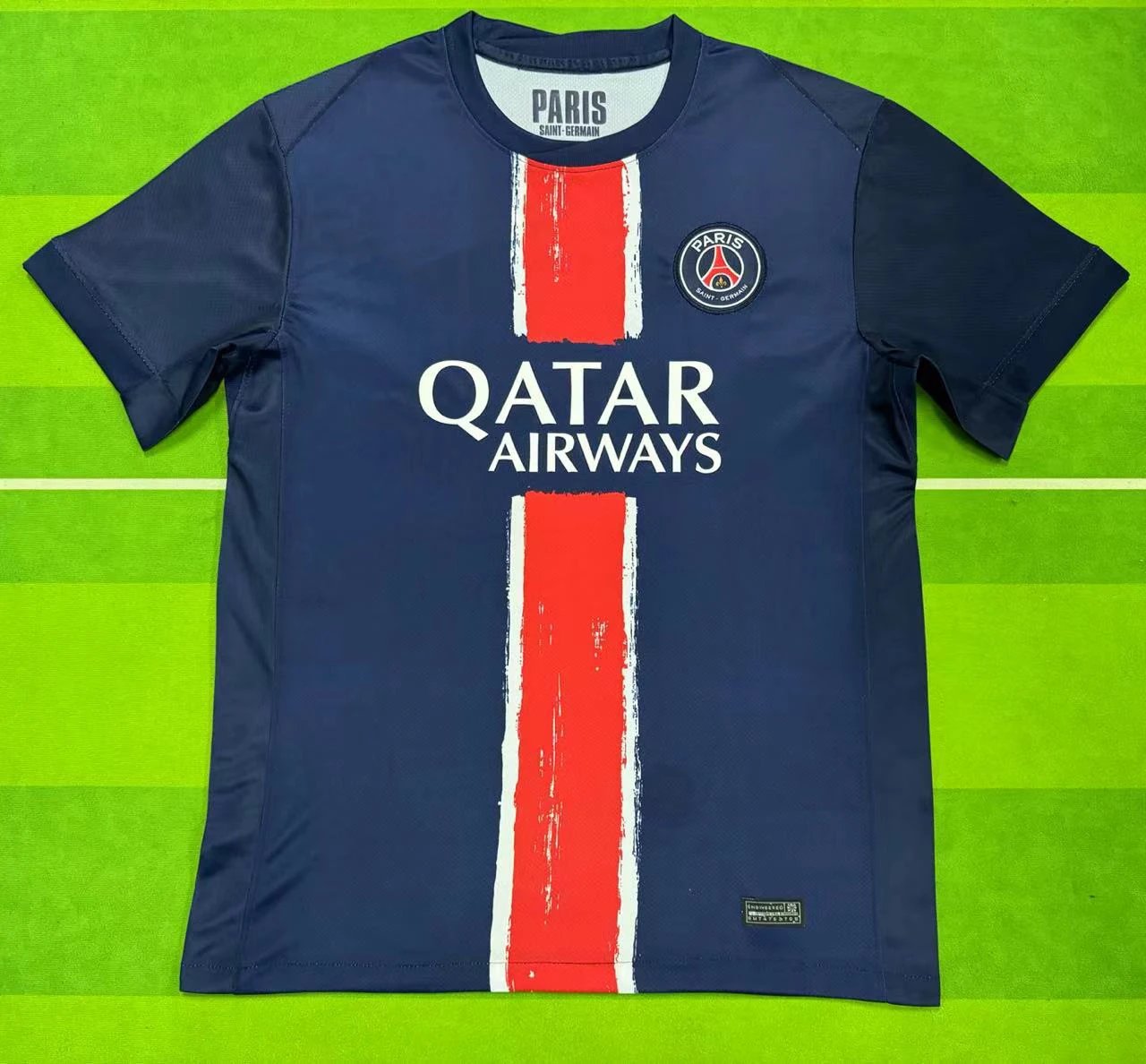 Navy blue sports jersey with red and white stripes on a green background