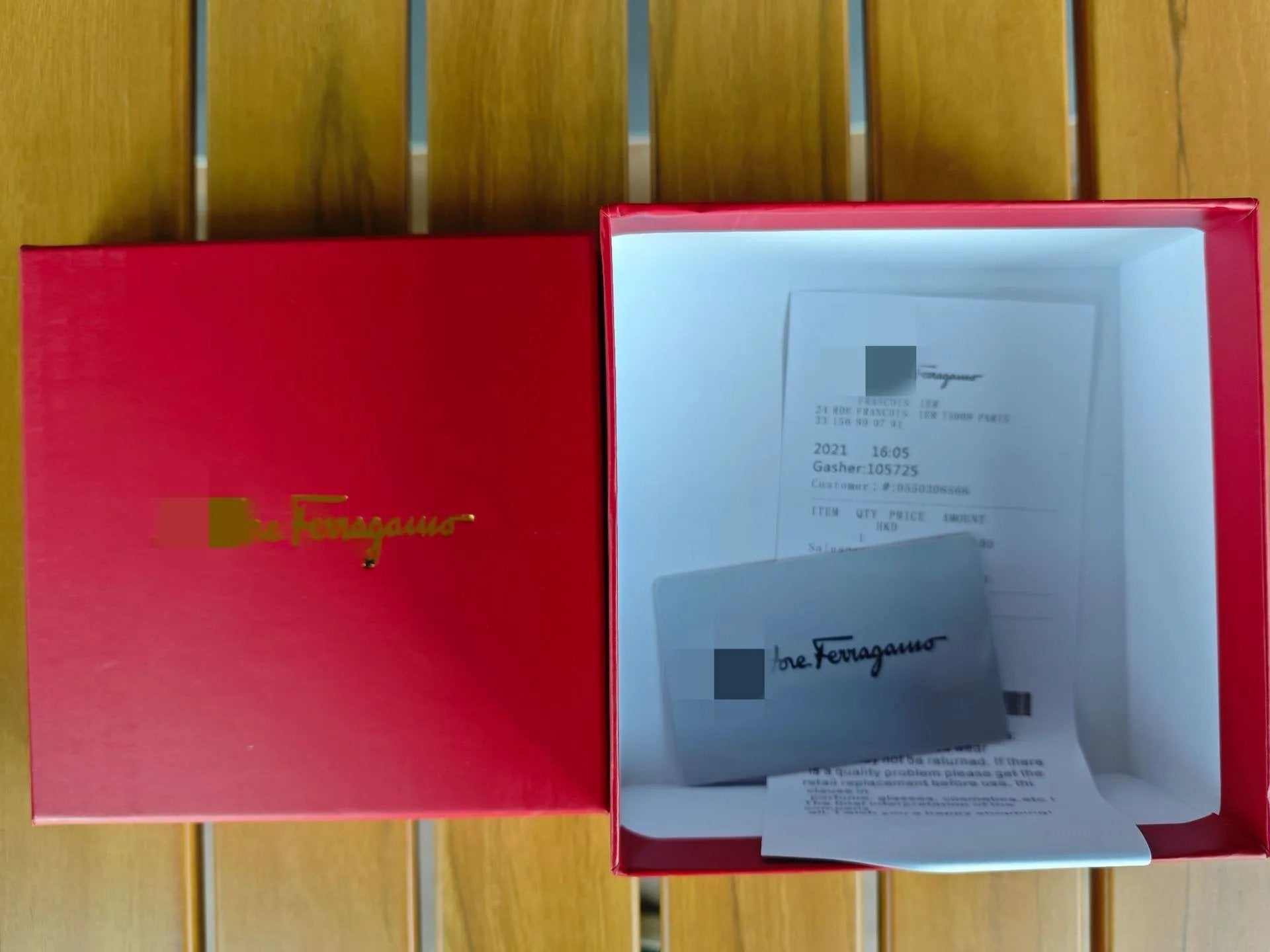 Red box with Salvatore Ferragamo branding, containing a silver card and paper on a wooden surface.