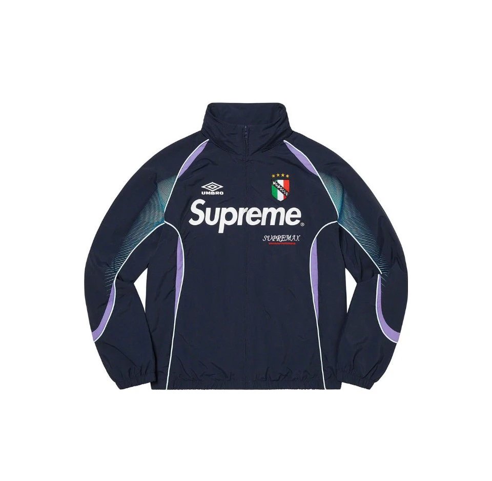 A navy blue zip-up windbreaker jacket featuring a high collar, a large white Supreme logo on the chest, a small Umbro logo above it, and a crest with four stars. The jacket has light purple and teal accent panels on the shoulders and sides, and is displayed flat against a solid white background.