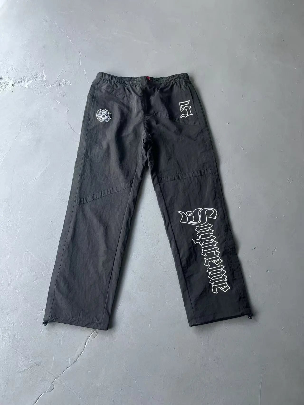 Black cargo pants with white graphic prints, laid flat on a gray concrete floor.