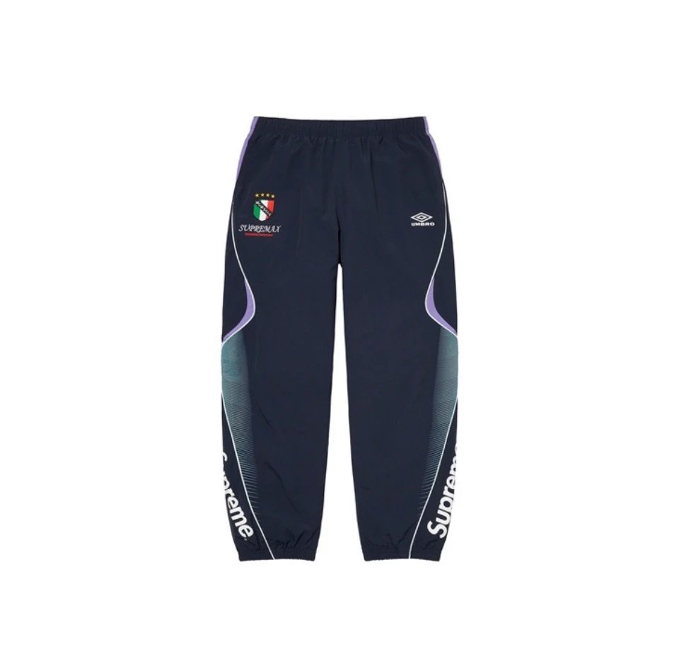A pair of navy blue track pants with purple side panels, featuring the Italian national team crest on the left thigh and the Umbro logo on the right thigh, displayed against a plain white background.