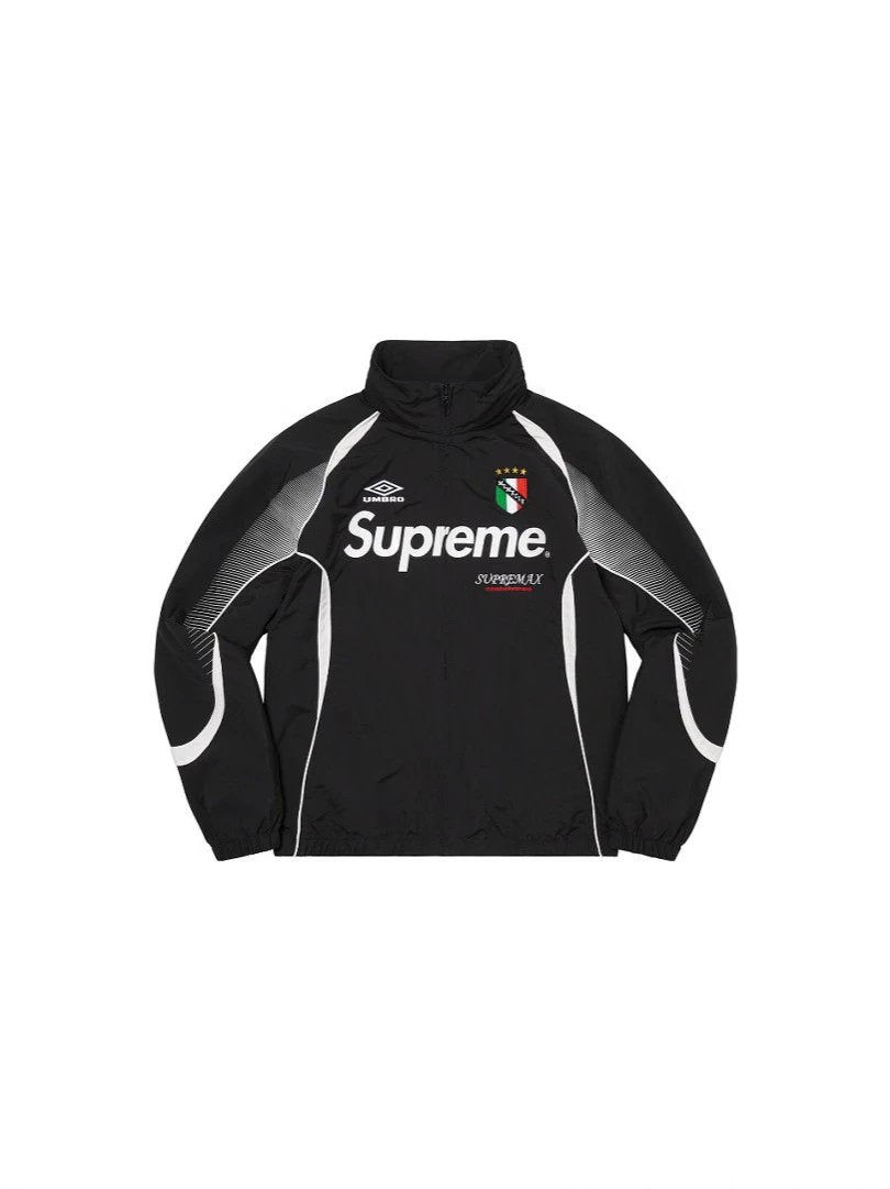 A black zip-up track jacket featuring a high collar, with 'Supreme' printed in white across the chest, an Umbro logo on the right chest, and a red, white, and green Italian flag crest on the left chest. The jacket has gray and white patterned panels on the sleeves.