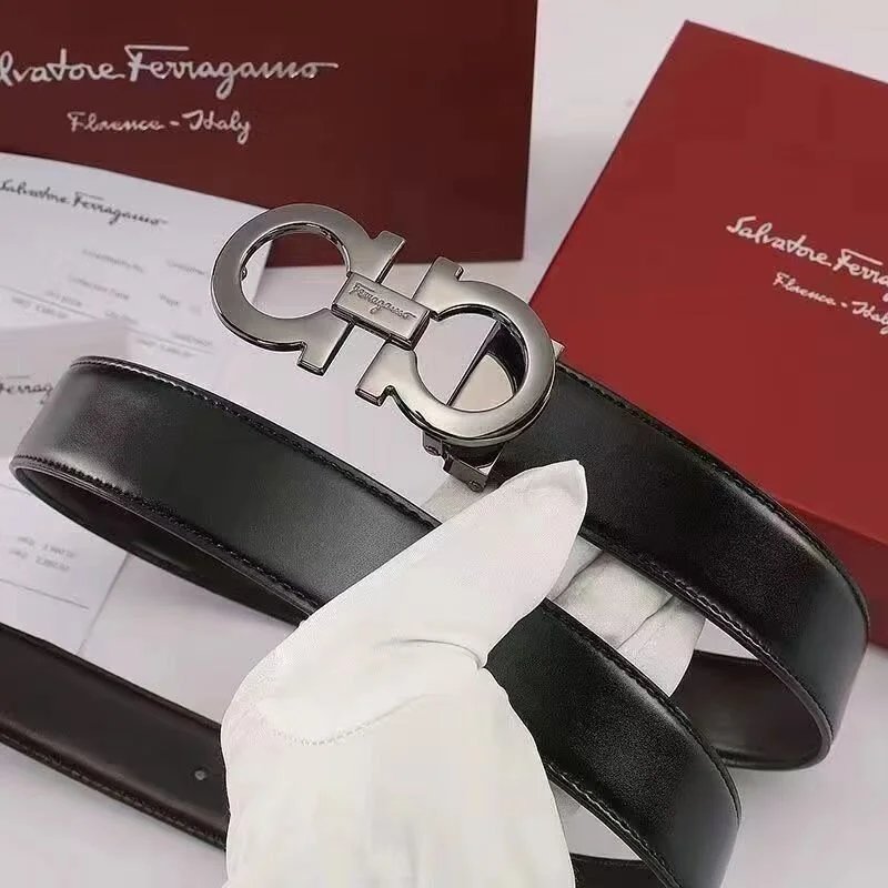 Black Salvatore Ferragamo belt with silver buckle held by a gloved hand, with brand packaging in the background.