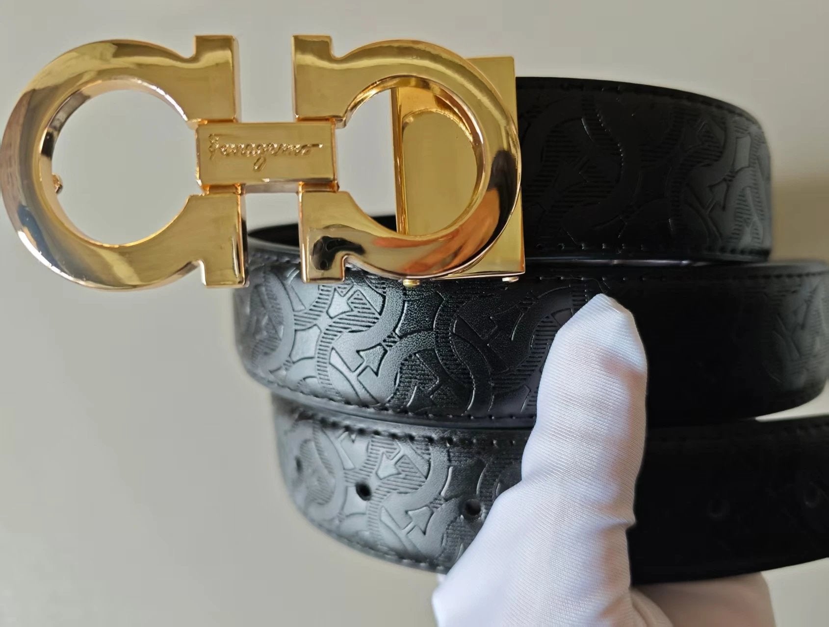 Black belt with gold buckle held by a gloved hand against a neutral background