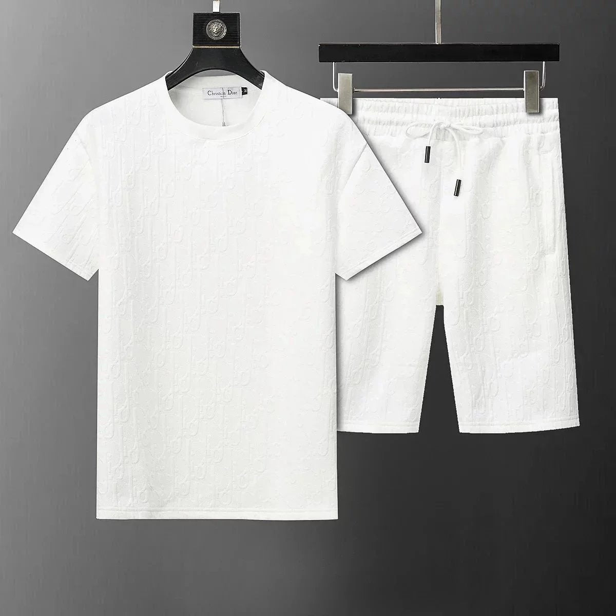 White t-shirt and shorts set with subtle pattern on hangers against a dark background