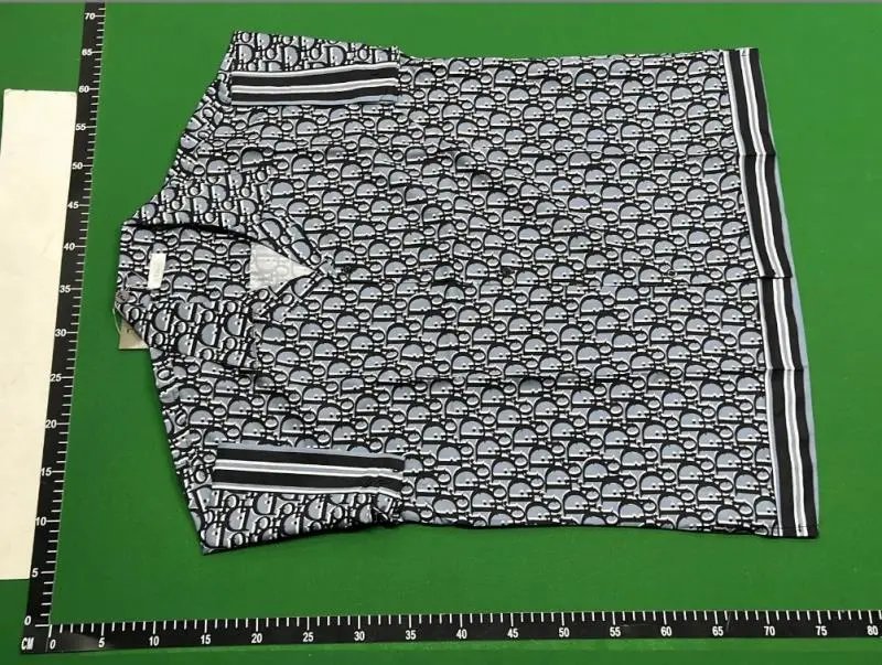Folded polo shirt with black and white pattern on a green surface with ruler for scale.