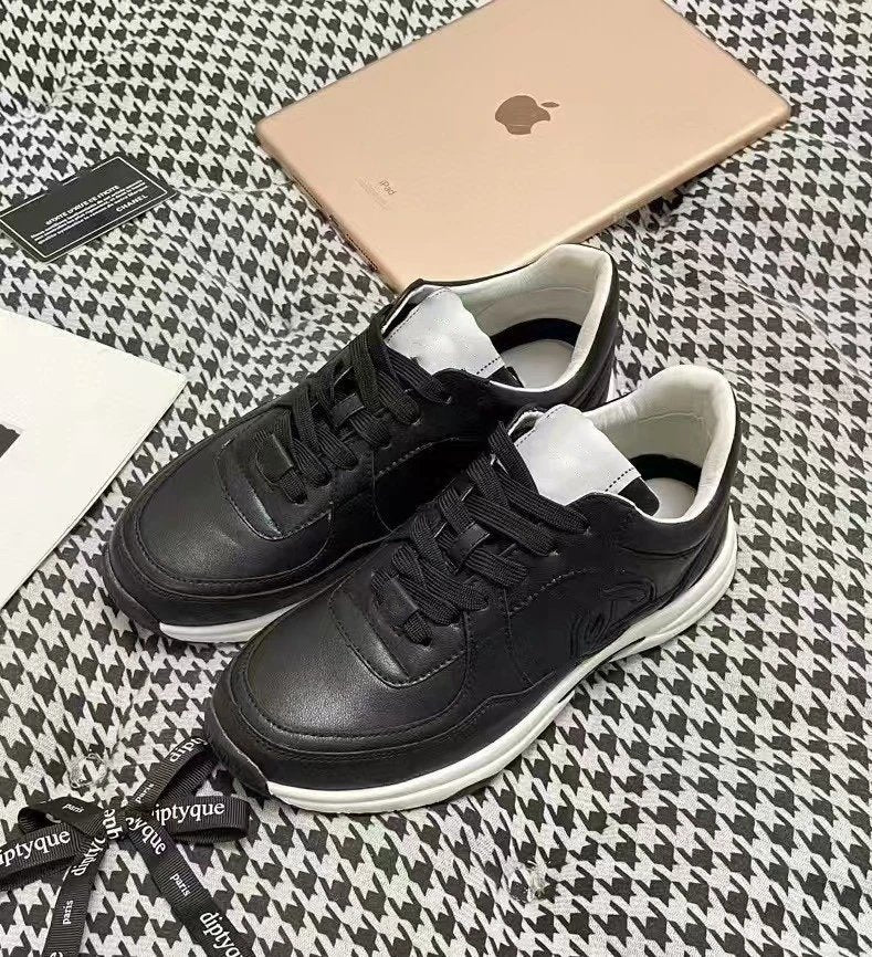 Black sneakers with white soles on a patterned surface, next to an Apple product and a branded strap.