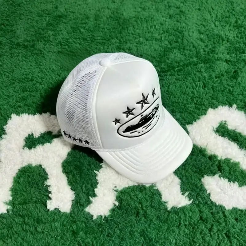 A white trucker-style cap with black embroidered stars and a circular graphic on the front, resting on a green and white textured rug.