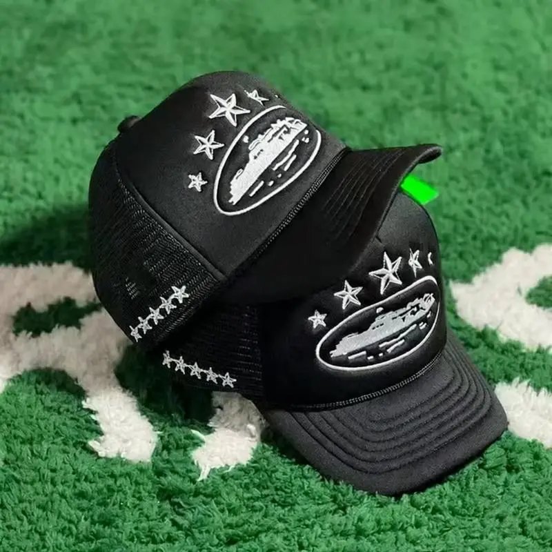 Two black trucker hats with white embroidered star and ship designs, displayed on a green and white textured rug.