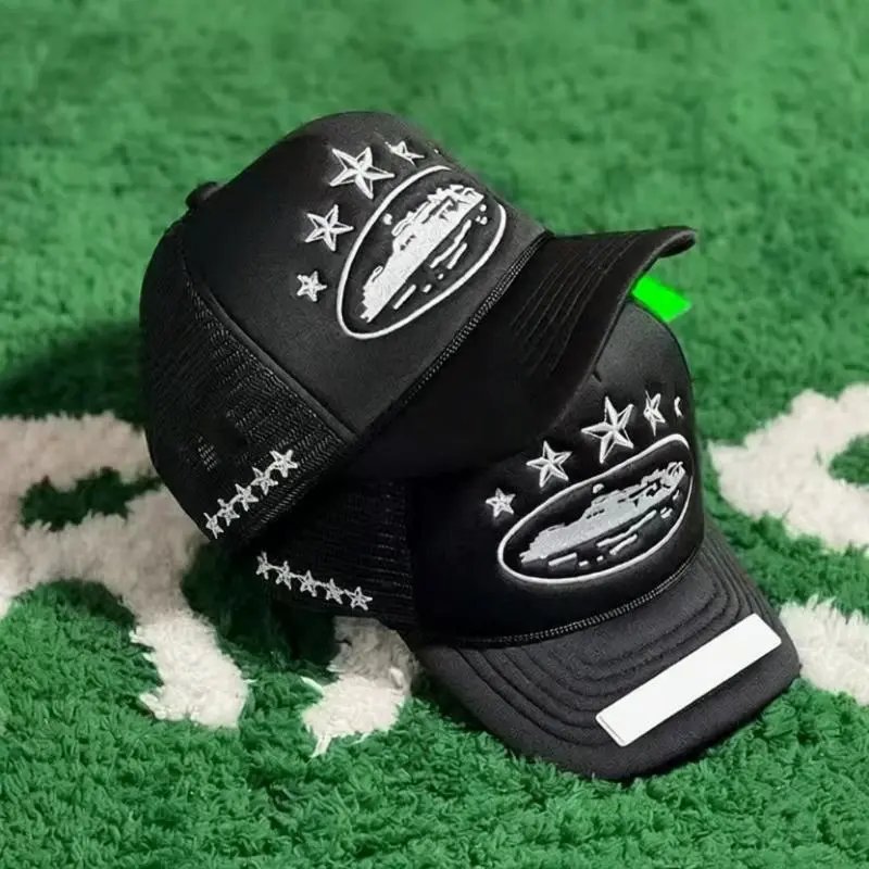 Two black trucker hats with embroidered white ship and star designs, displayed on a green and white textured rug.
