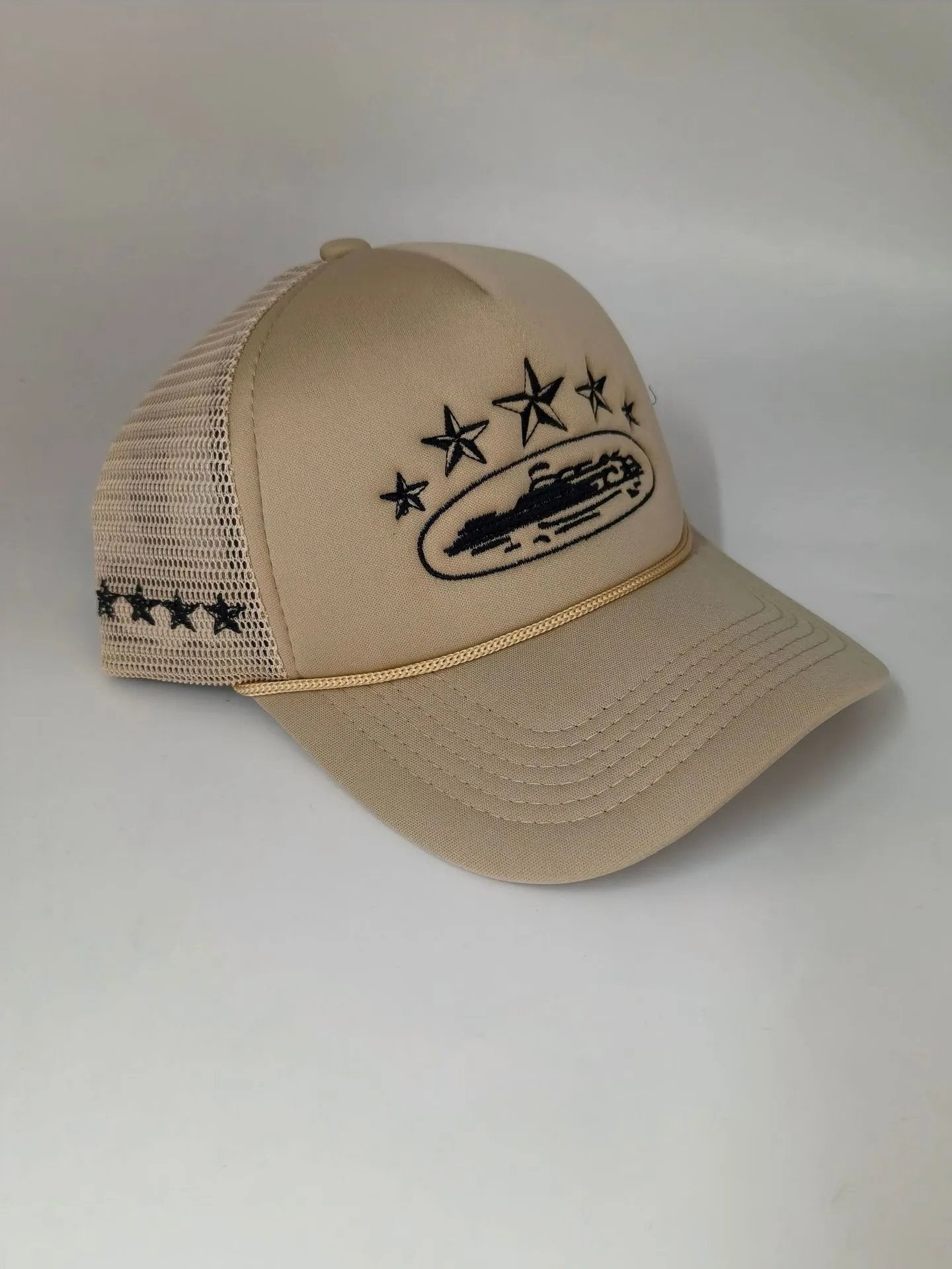 A beige trucker hat with black embroidered stars, a boat graphic, and a gold-toned mesh band on the side, displayed against a plain light gray background.