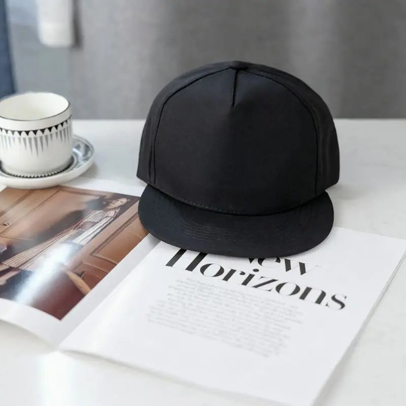 A black baseball cap resting on an open magazine page on a white tabletop, with a cup and saucer in the background.