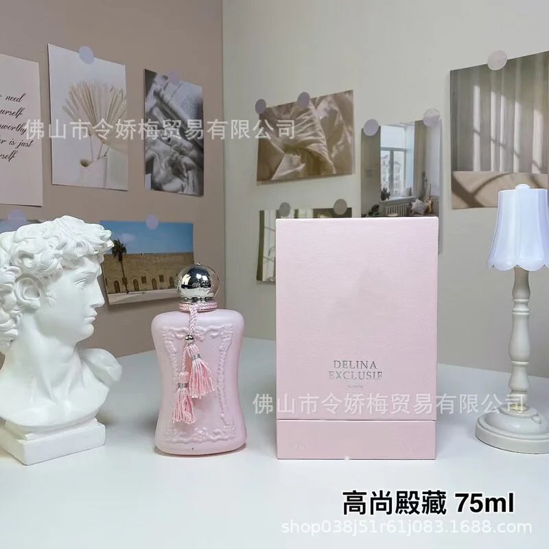 Pink perfume bottle with decorative elements on a white surface, surrounded by framed pictures and a lamp.