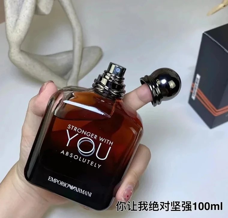 Brown perfume bottle with 'Stronger with You Absolutely' text held by a hand, with a white background.