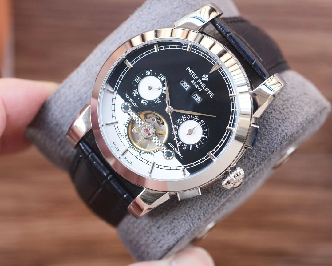 Luxury watch with black face and leather strap held by a hand on a wooden surface