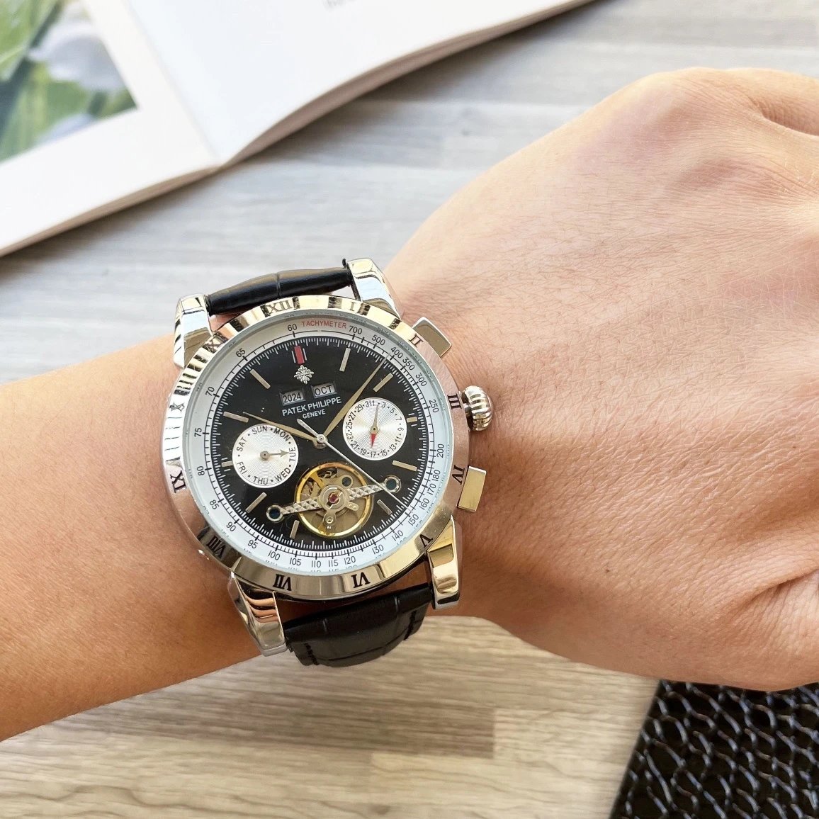 Luxury watch with black strap and gold casing on a wrist, blurred background