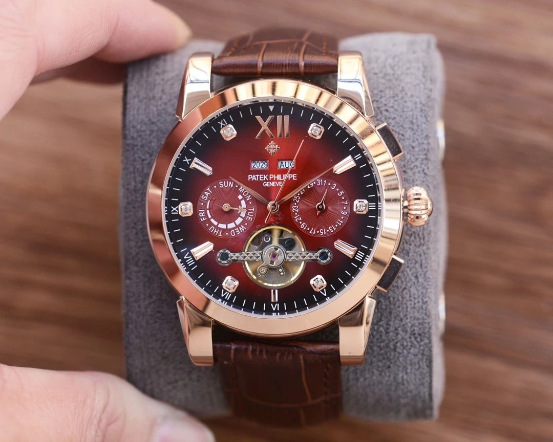 Luxury watch with brown leather strap and red face on a gray cushion, held by a hand.