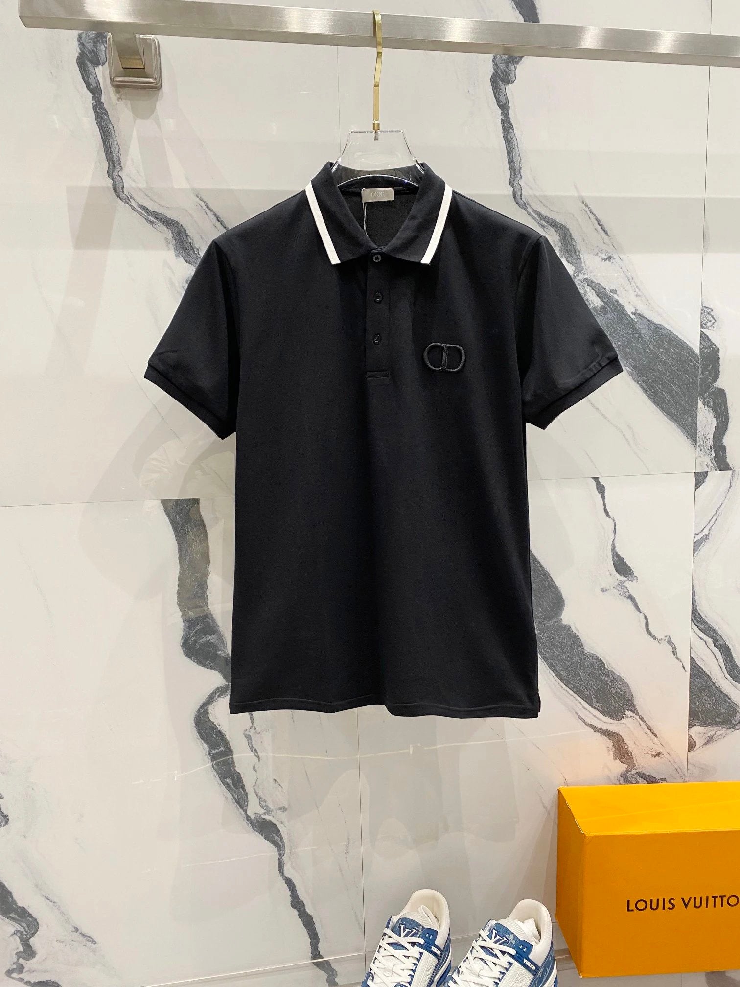 Black polo shirt with a logo on a marble background with a Louis Vuitton box.
