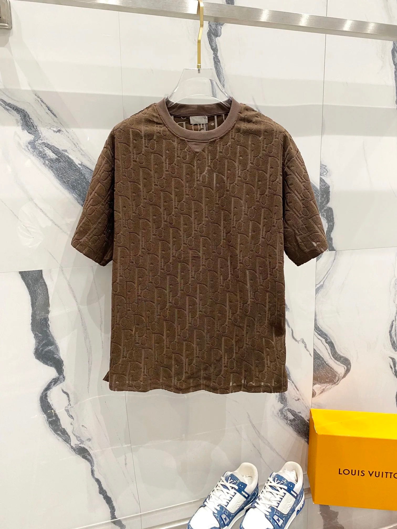 Brown textured t-shirt on a hanger with a Louis Vuitton sneaker and box in the background.
