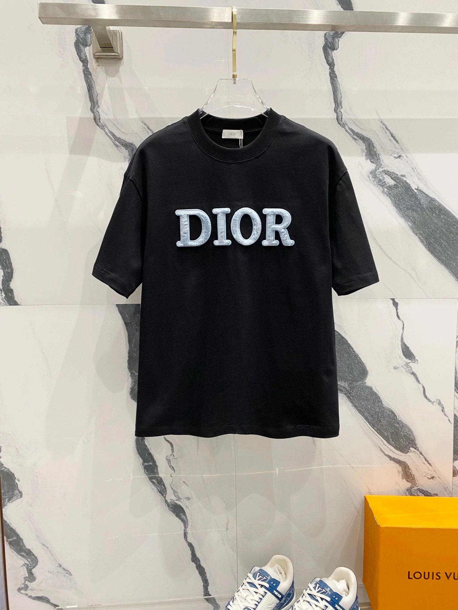 Black Dior t-shirt on a hanger against a marble wall.