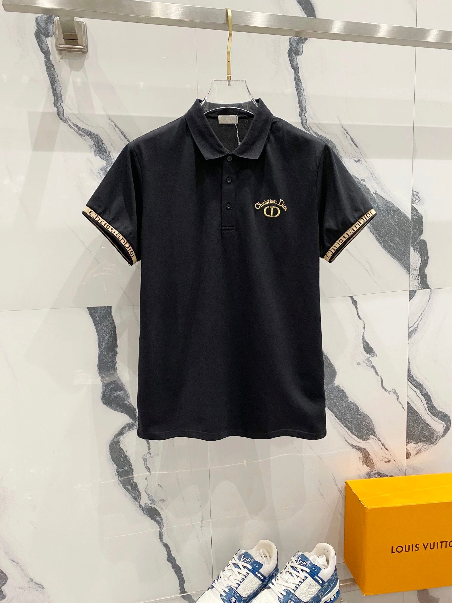 Black polo shirt with gold accents on a marble background, featuring a Louis Vuitton box.