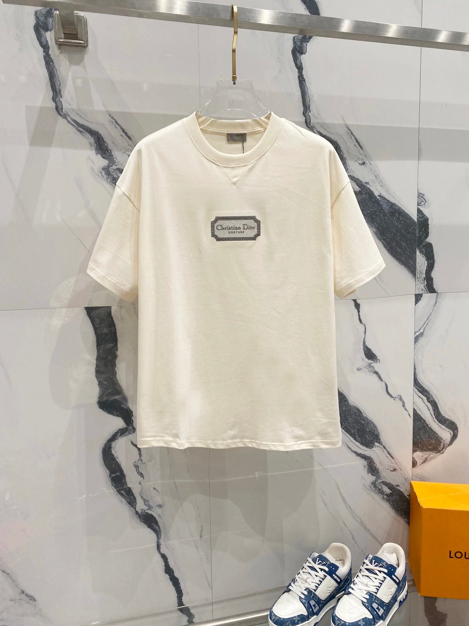 White t-shirt with a logo on a hanger against a marble wall.