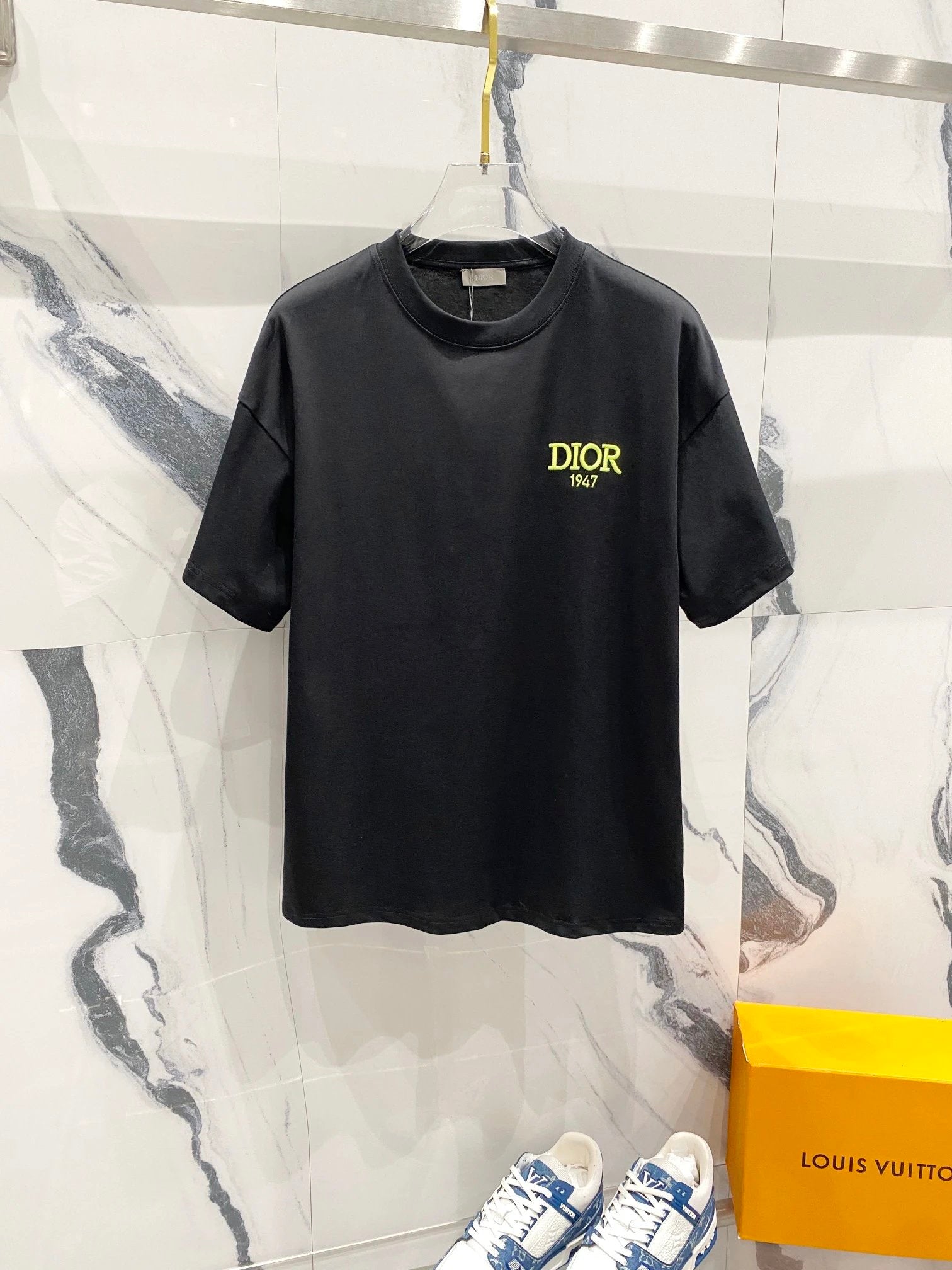 Black t-shirt with 'Dior' logo on a marble surface with a Louis Vuitton box.
