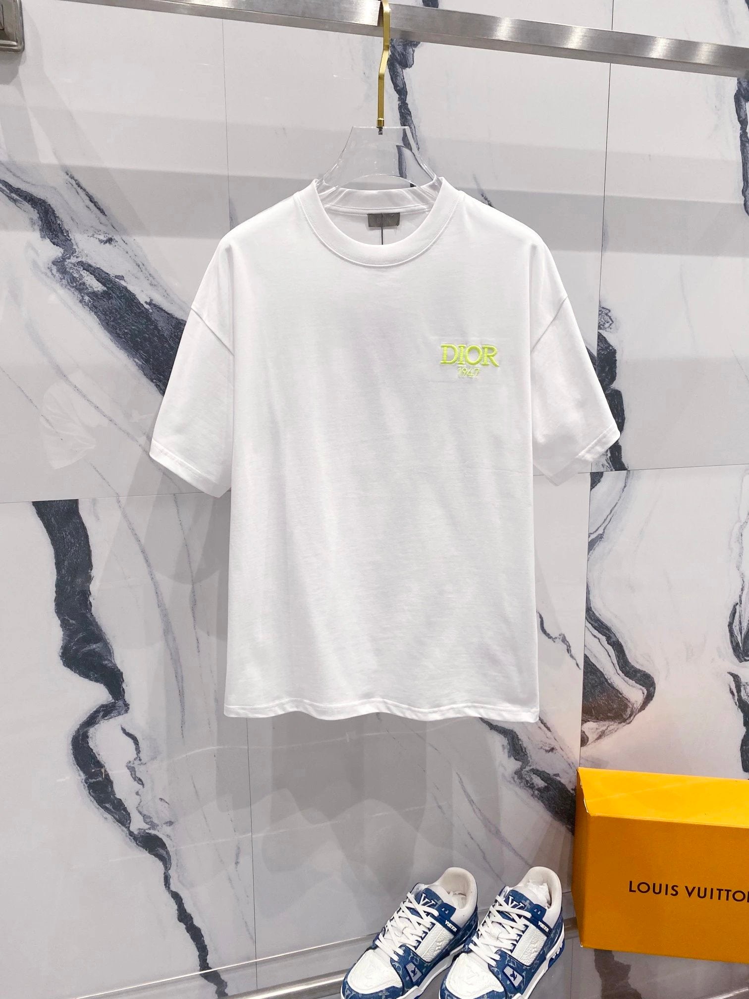 White t-shirt with a logo and blue sneakers on a marble floor with a Louis Vuitton box.