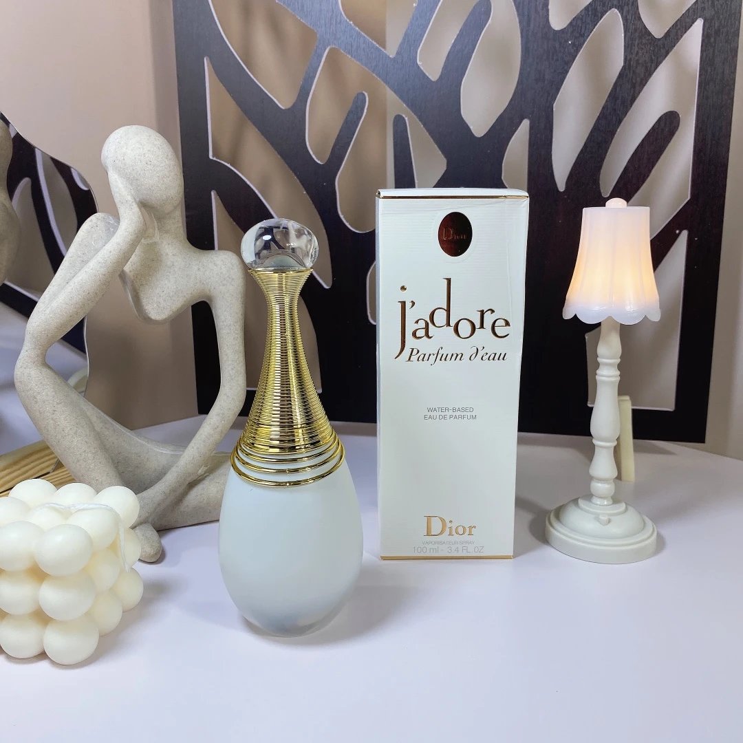 Dior Jadore perfume bottle and packaging on a decorative surface with a lamp and sculpture.