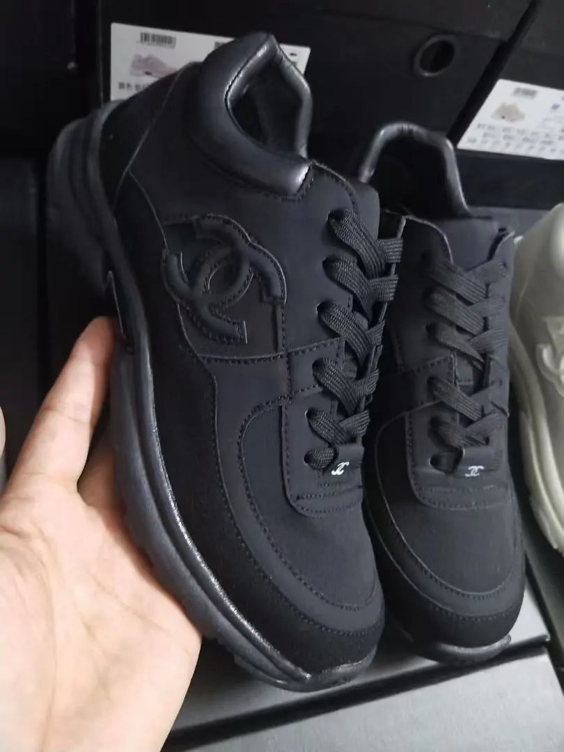 Black sneakers with a logo held by a hand, displayed on a black surface.